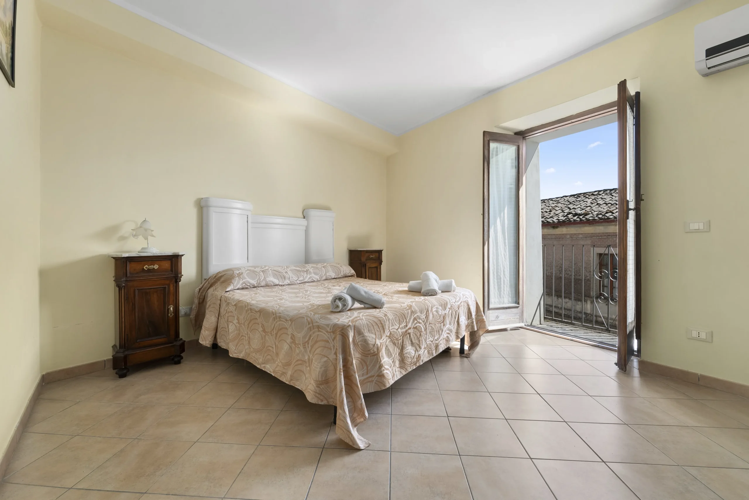 camera dell'albergo diffuso, letto matrimoniale con sopra poggiati degli asciugamani accuratamente arrotolati, finestra aperta con il sole che entra
