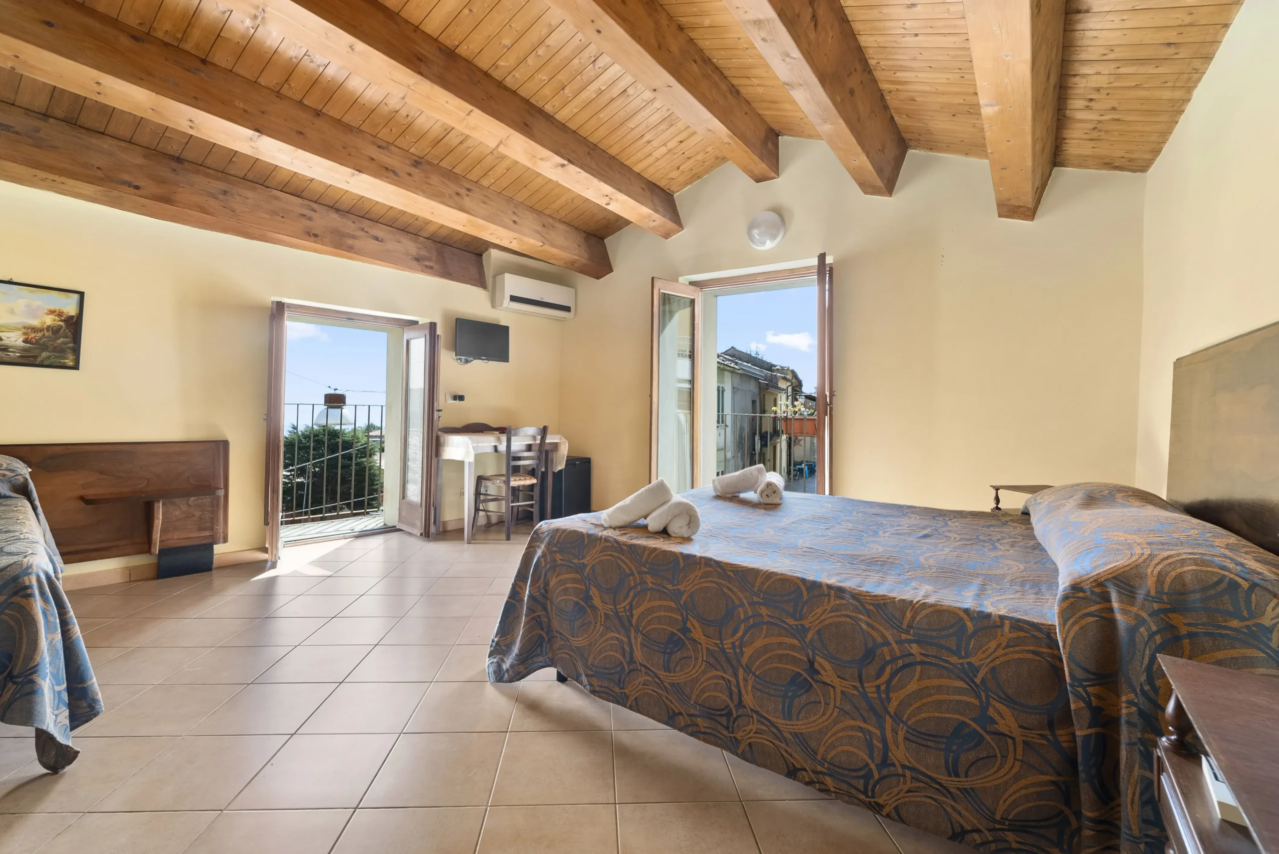 camera dell'albergo diffuso, due letti con sopra poggiati degli asciugamani accuratamente arrotolati, finestra aperta con il sole che entra